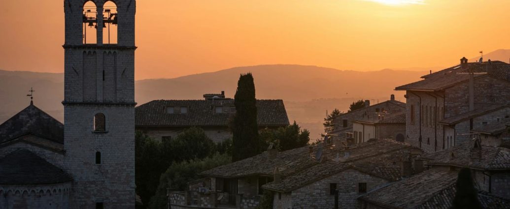 Stunning sunset over the historic stone buildings of Assisi, Italy with a bell tower in view.