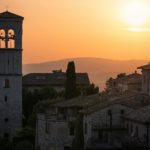 Stunning sunset over the historic stone buildings of Assisi, Italy with a bell tower in view.