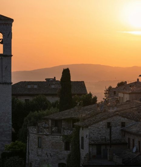 Stunning sunset over the historic stone buildings of Assisi, Italy with a bell tower in view.