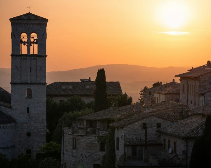 Stunning sunset over the historic stone buildings of Assisi, Italy with a bell tower in view.